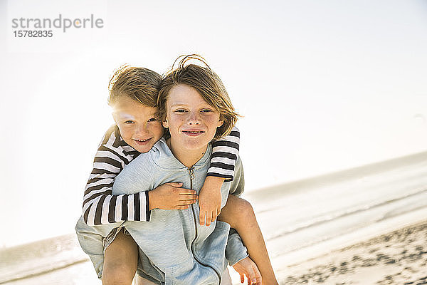 Porträt eines Jungen  der seinen Bruder huckepack am Strand trägt