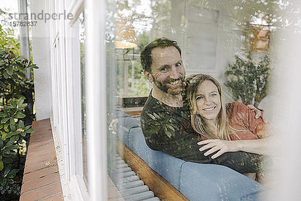 Glückliches Paar auf der Couch sitzend  mit Arns um sich herum  lächelnd