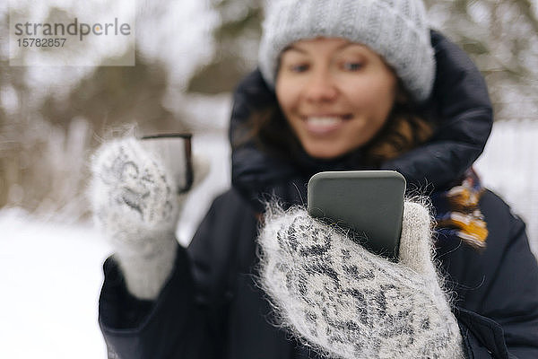 Frau mit Thermobecher  die im Winter mit dem Smartphone Selbstgespräche führt