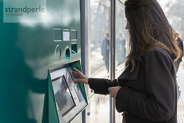 Junge Frau benutzt Fahrkartenautomat an Straßenbahnhaltestelle