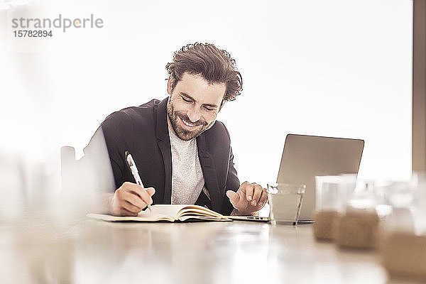 Junger Mann in Business-Jacke arbeitet an einem Laptop und macht Notizen in einem Strandhaus