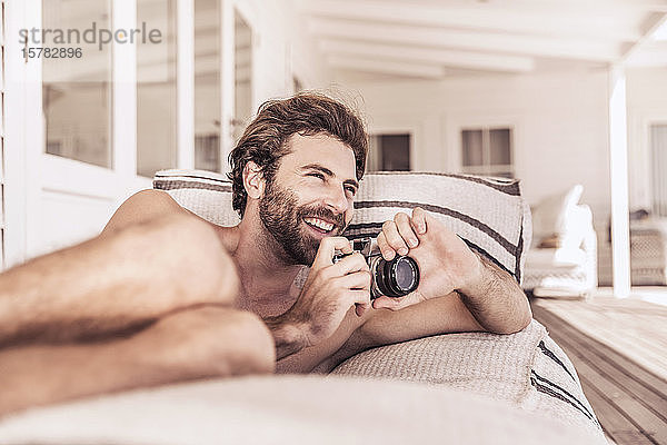 Fröhlicher junger Mann mit Oldtimer-Kamera entspannt auf einer Veranda