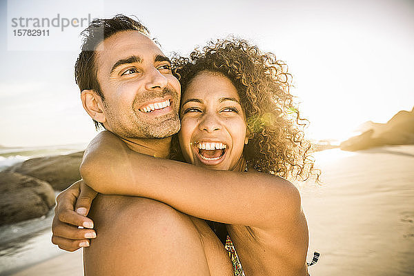 Sorgenfreies Paar umarmt sich am Strand bei Sonnenuntergang