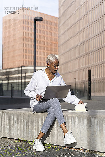 Lässige Geschäftsfrau  die in der Stadt sitzt und einen Laptop benutzt