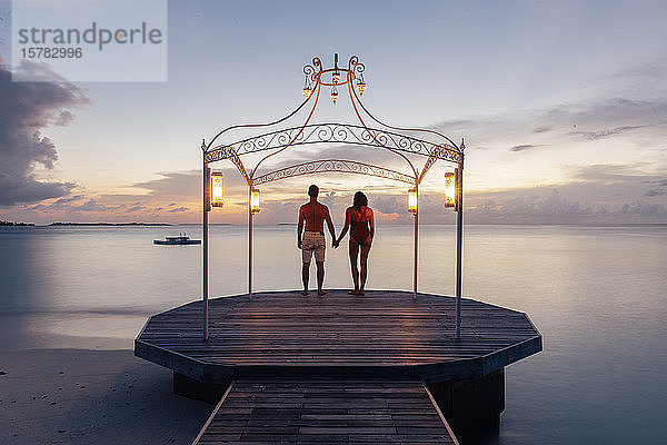 Ehepaar steht bei Sonnenuntergang auf einem Steg am Meer  Insel Maguhdhuvaa  Gaafu-Dhaalu-Atoll  Malediven
