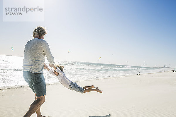 Vater amüsiert sich mit seinem Sohn am Strand und dreht ihn herum