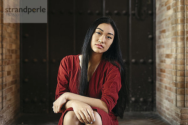 Porträt einer schönen jungen Frau in einem roten Kleid  die vor einer Tür sitzt
