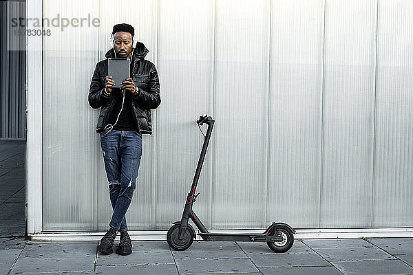 Mann mit Kopfhörer  Tablet und E-Scooter im Freien