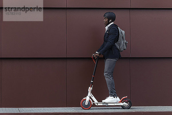 Geschäftsmann mit Rucksack und Fahrradhelm auf Schubscooter