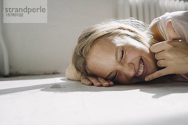 Porträt einer glücklichen blonden jungen Frau auf dem Boden liegend