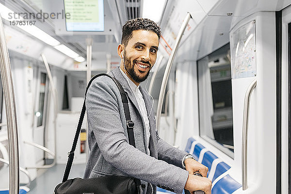 Porträt eines lächelnden jungen Geschäftsmannes mit Kopfhörern in der U-Bahn