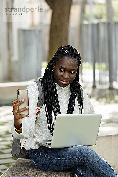Studentin benutzt Laptop und Mobiltelefon auf einer Bank