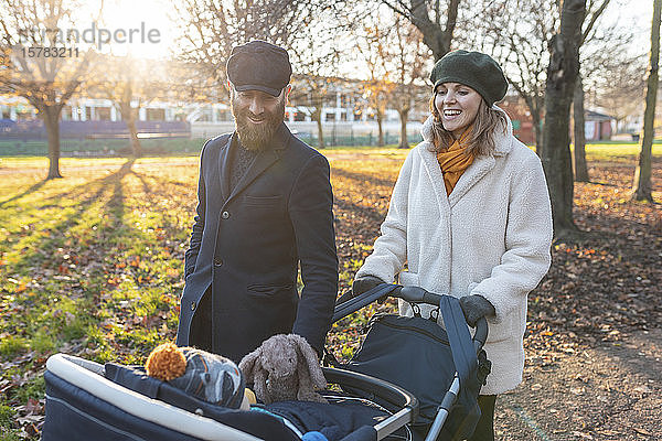 Glückliches Paar mit kleinem Sohn in einem Kinderwagen im Park