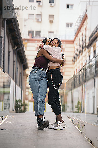 Zwei glückliche junge Frauen umarmen sich in der Stadt
