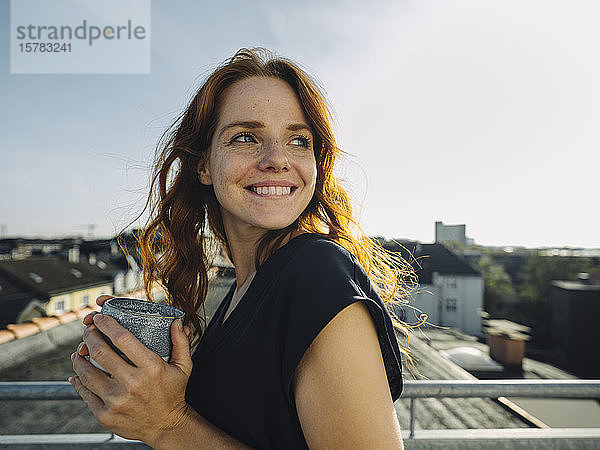Lächelnde rothaarige Frau bei einer Kaffeepause auf der Dachterrasse