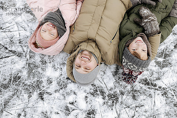 Familienporträt von Vater und zwei Kindern  die im Winter auf Eis liegen