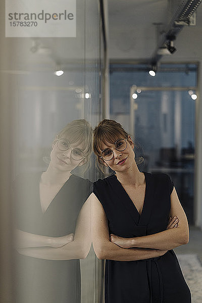 Porträt einer an eine Glasscheibe gelehnten Geschäftsfrau im Büro