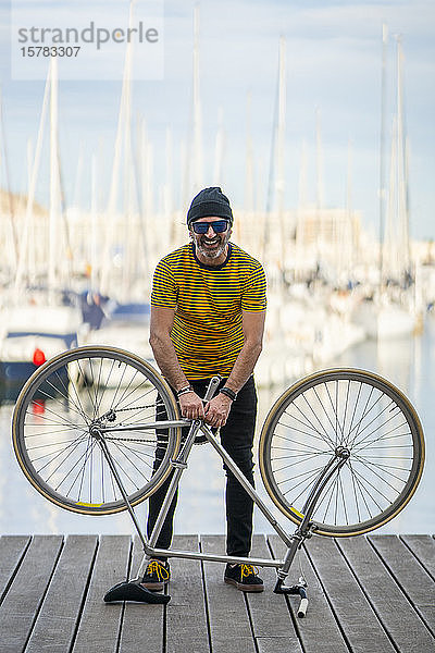 Porträt eines lachenden  reifen Mannes mit einem Fixie-Rad  stehend auf einer Promenade  Alicante  Spanien