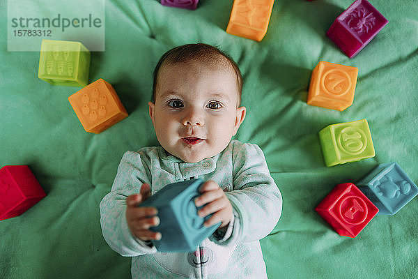 Porträt eines kleinen Mädchens  das auf einer grünen Matte liegt und mit Gummispielzeug spielt