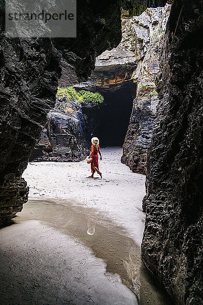 Blonde Frau in rotem Kleid und Hut in einer Felshöhle  Playa de Las Catedrales  Spanien