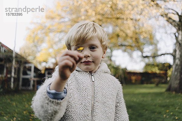 Porträt eines Jungen mit winzigem Herbstblatt im Garten