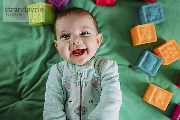 Porträt eines fröhlichen Mädchens auf grüner Matte liegend mit Gummispielzeug