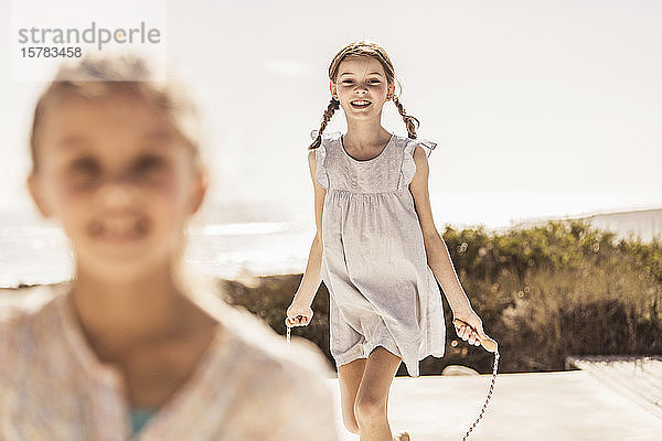 Glückliches Mädchen spielt mit Springseil auf der Terrasse eines Strandhauses