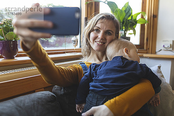 Frau nimmt einen Selfie mit ihrem niedlichen schlafenden Sohn auf dem Sofa