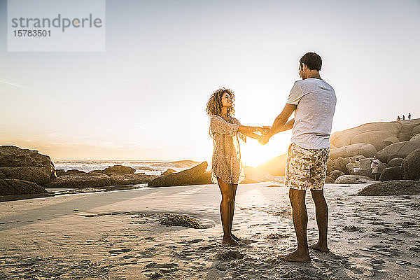 Glückliches Paar hält sich bei Sonnenuntergang am Strand an den Händen