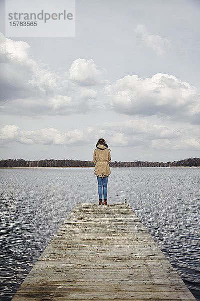 Rückenansicht einer Frau  die auf einem Steg steht und auf den See schaut