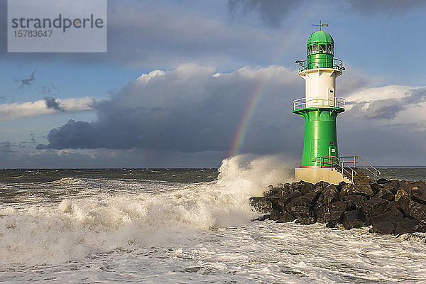 Deutschland  Mecklenburg-Vorpommern  Warnemünde  Regenbogen über Leuchtturm und gegen Felsen schlagende Meereswellen