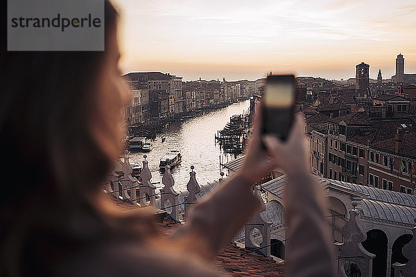 Junge Frau beim Fotografieren mit dem Handy auf einem Balkon über der Stadt Venedig  Italien