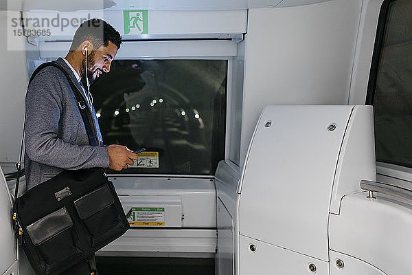 Junger Geschäftsmann mit Handy und Kopfhörern in der U-Bahn