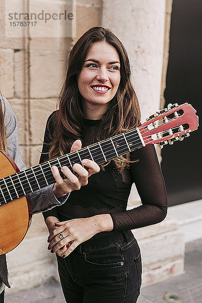 Porträt einer lächelnden jungen Frau mit einem Gitarre spielenden Mann in der Stadt