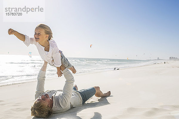 Vater amüsiert sich mit seinem Sohn am Strand und tut so  als würde er fliegen