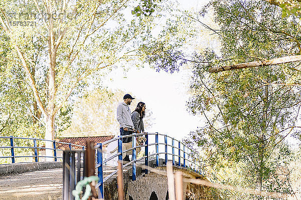 Ein Paar mit seinem Hund steht auf einer Brücke in einem Park