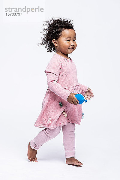 Porträt eines barfüssigen kleinen Mädchens in rosa gekleidet  das vor weissem Hintergrund geht