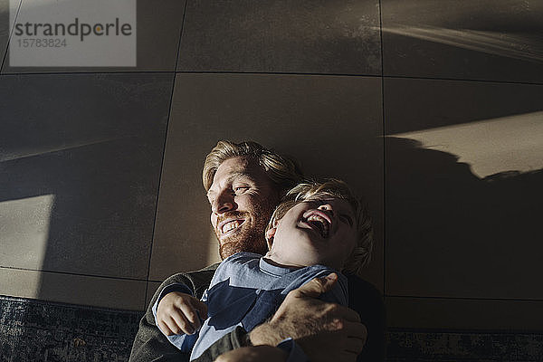 Glückliche Vater und Sohn kuscheln zu Hause auf dem Boden
