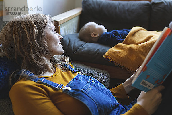 Frau liest Buch im Wohnzimmer  während der kleine Sohn schläft