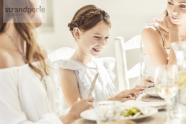 Glückliches Mädchen und zwei Frauen essen zusammen zu Mittag