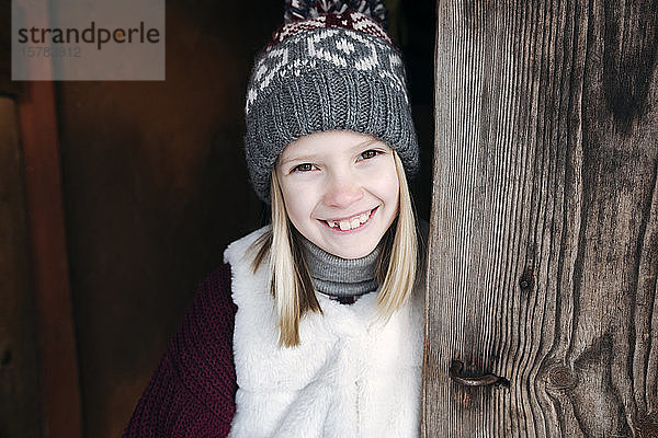 Porträt eines glücklichen Mädchens mit Wollhut an Holzwand