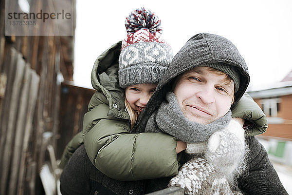 Porträt eines Vaters  der seine Tochter im Winter huckepack im Freien trägt