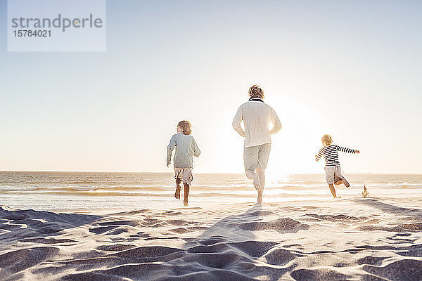 Vater amüsiert sich mit seinen Söhnen am Strand  rennt im Sand