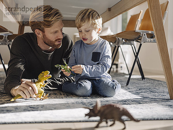 Vater und Sohn spielen zu Hause mit Dinosaurierfiguren unter dem Tisch