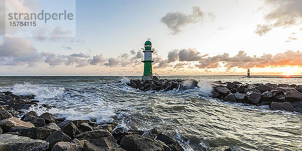 Deutschland  Mecklenburg-Vorpommern  Warnemünde  Leuchtturm und Meereswellen  die bei Sonnenuntergang gegen Felsen schlagen