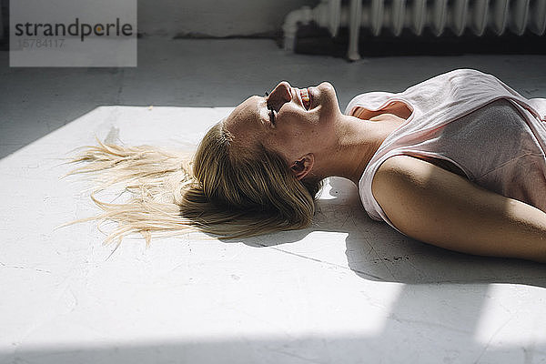 Lächelnde blonde junge Frau  die im Sonnenlicht auf dem Boden liegt