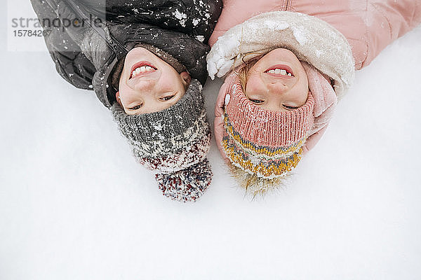 Porträt von zwei lächelnden Geschwistern auf Schnee liegend