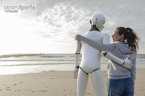 Lächelnde Frau steht Arm in Arm mit Roboter am Strand