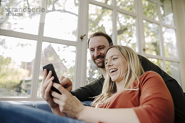 Lachendes Paar benutzt Smartphone zu Hause