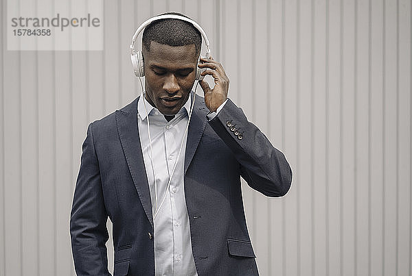 Porträt eines jungen Geschäftsmannes mit geschlossenen Augen beim Musikhören mit Kopfhörern im Freien